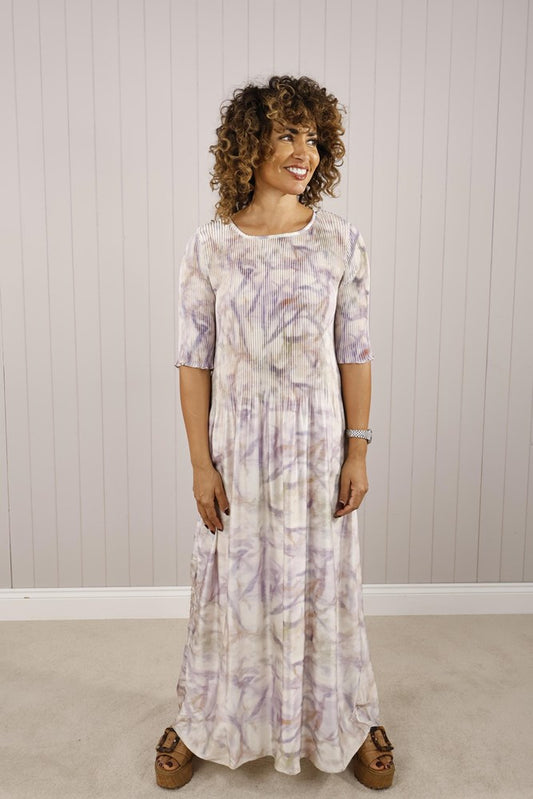 A woman wearing a floral pleated shirred bust dress with 3/4 sleeves, in a light green and multicolor pattern, suitable for occasion wear such as weddings or christenings.